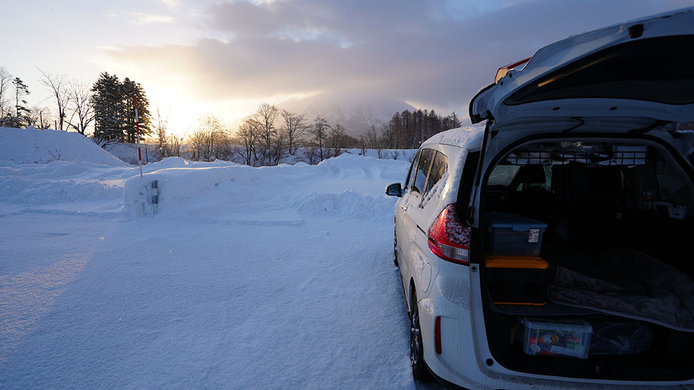 雪の中で車中泊で一夜を明かして朝日を見ている写真